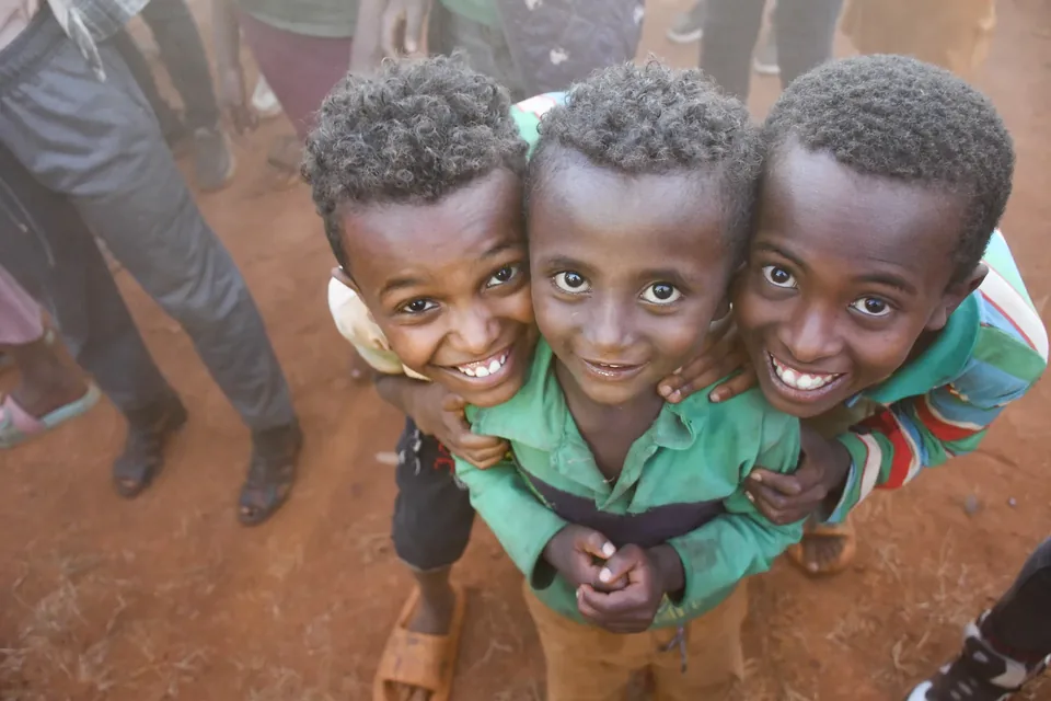 Three children smiling together in a photograph from the In His Name Ministries archive