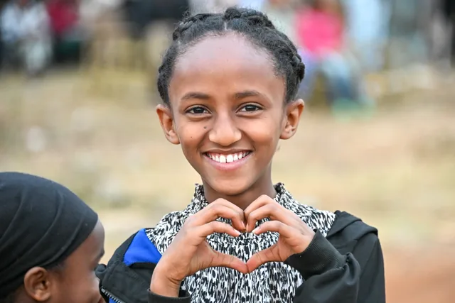 A young woman smiling and making a heart with her hands in a photograph from the In His Name Ministries archive